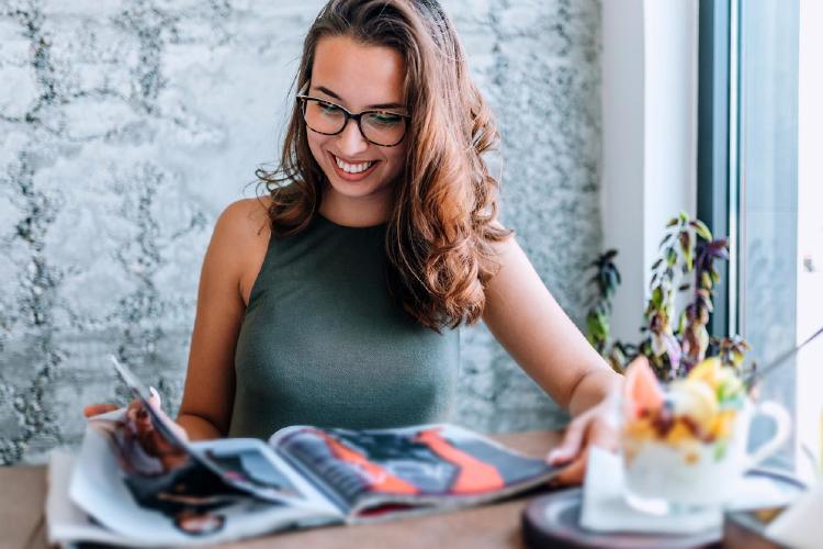 Mujer con gafas leyendo revista cerca de la ventana Mujer con gafas leyendo revista cerca de la ventana