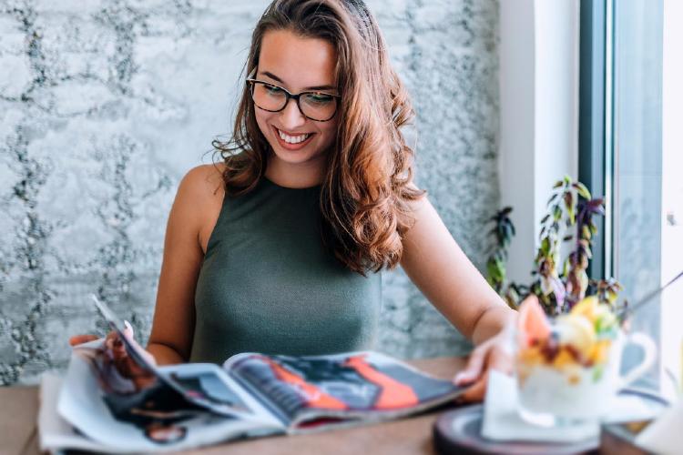 Mujer con gafas leyendo revista cerca de la ventana